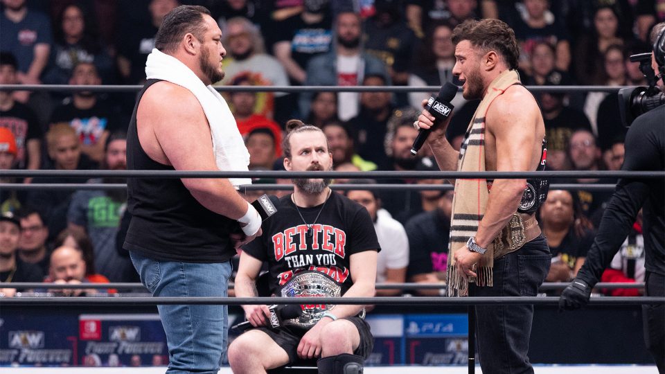 Samoa Joe (left) and MJF (right) face-off on AEW Dynamite as Adam Cole (center) watching on while sitting down