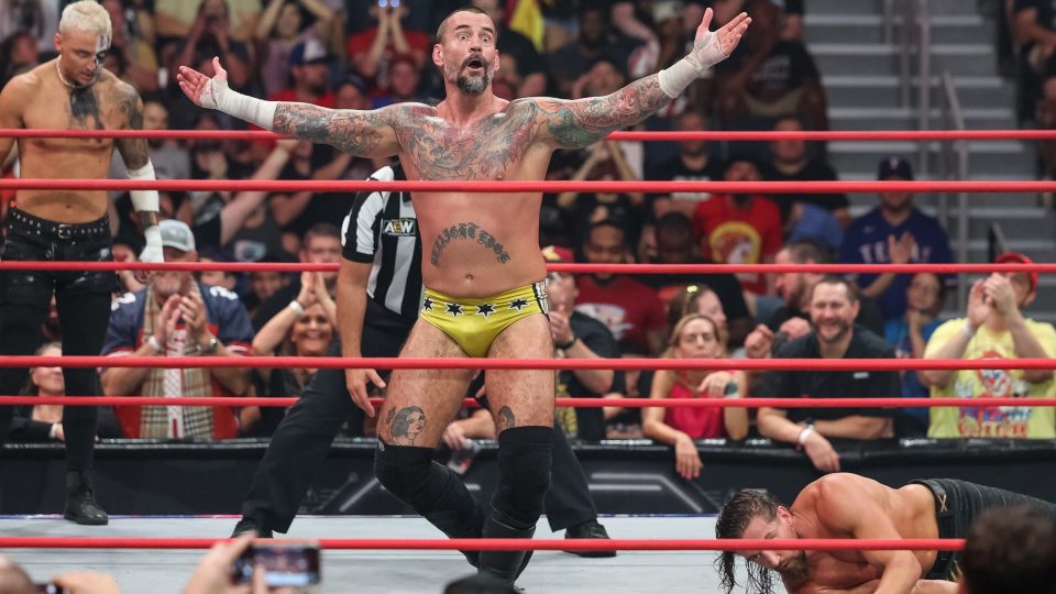 CM Punk taunts in the AEW Collision ring wearing yellow trunks.