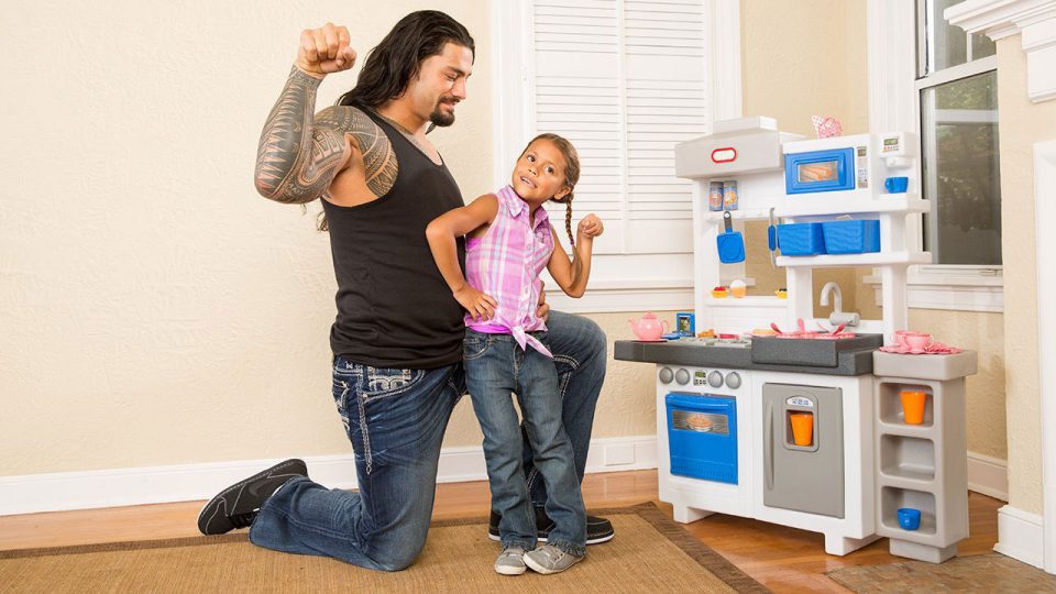 Roman Reigns poses with small child next to toy kitchen